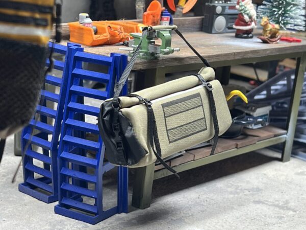 RC Scale Roll Top Tasche im Maßstab 1/10, beige mit schwarzen Details, realistisch gestaltet mit Rollverschluss und Schnallen, platziert in einer Modellbau-Werkstatt.